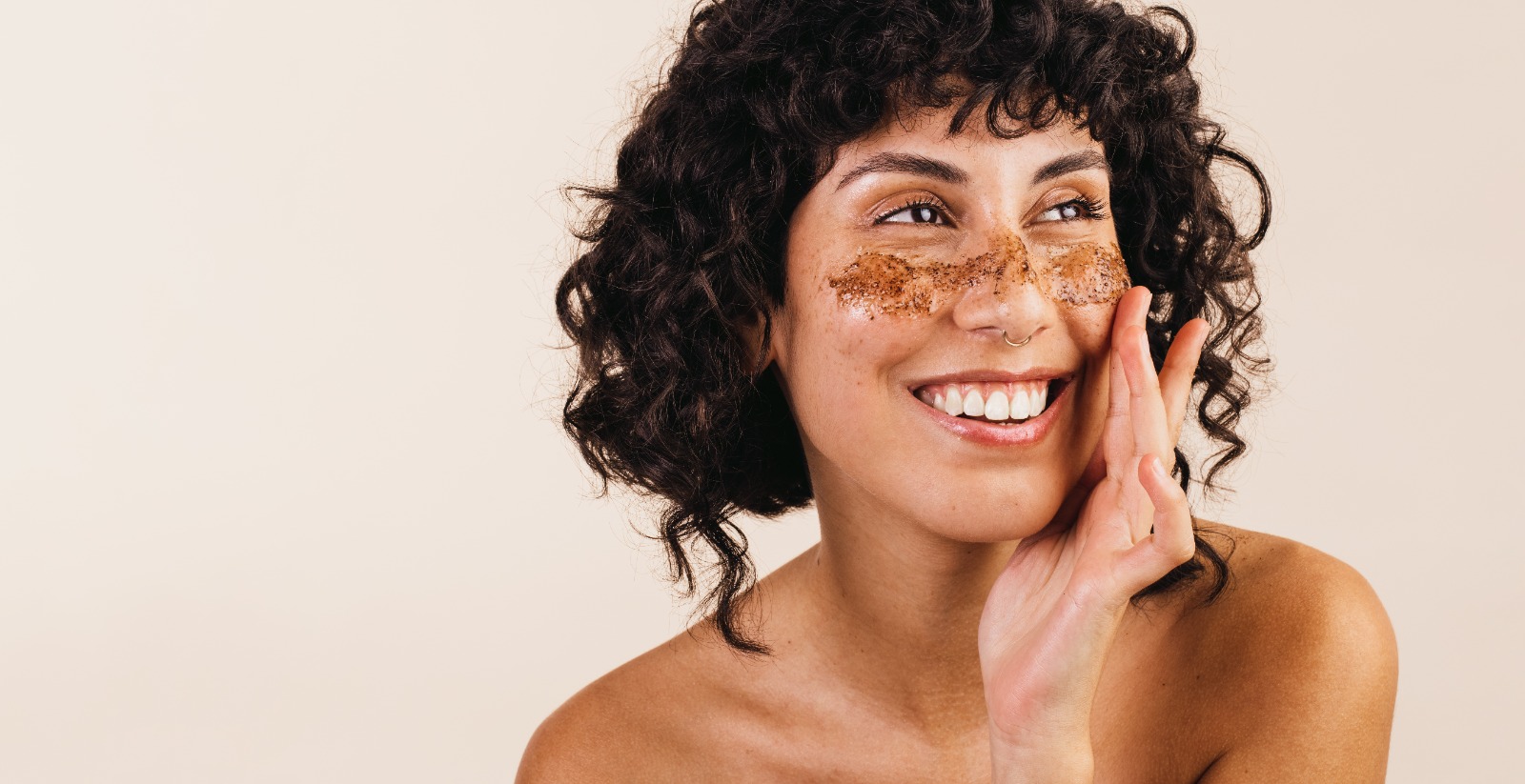 Woman with curly hair scrubs her face with a coffee scrub